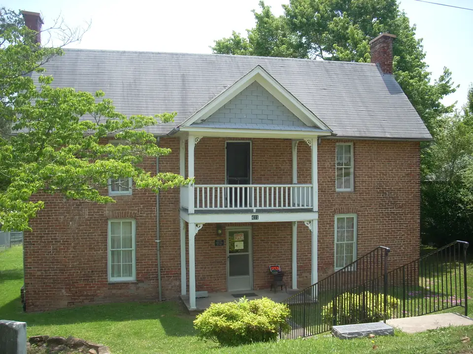 Two-story red-brick house with a gray roof, two chimneys, a white two-level front porch with balcony, house number 411, an 'OPEN' sign by the door and a black railing up a lawn