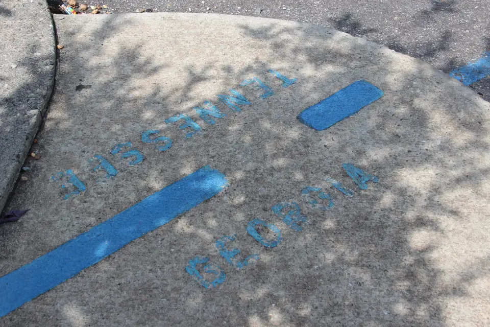 Painted blue stripe across a concrete sidewalk with stenciled 'TENNESSEE' and 'GEORGIA' on either side, in dappled shade