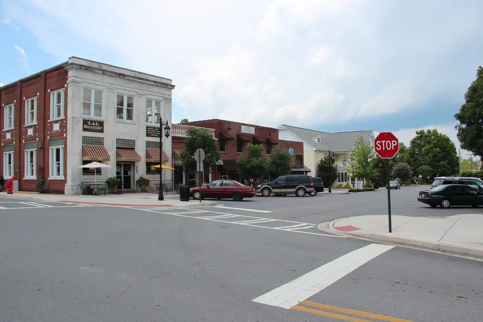 Two-story red-brick building with a white stone facade and striped awnings ('L&L Beanery' sign), cafe umbrellas, a row of brick shops and a white clapboard building, crosswalk and stop sign in the foreground