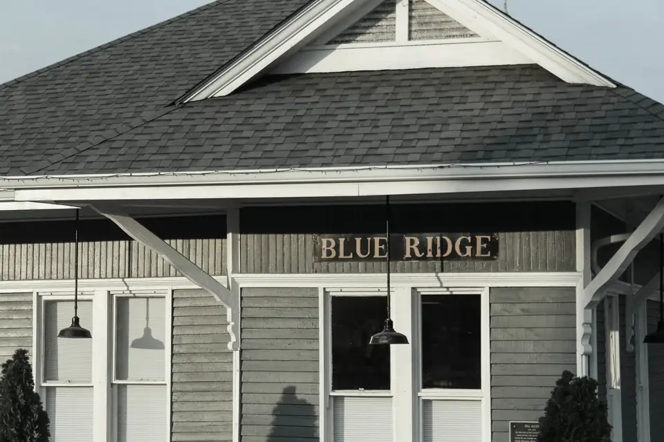 Black-and-white close view of a wooden depot facade with a 'BLUE RIDGE' sign, white brackets, pendant lamps and shingled roof