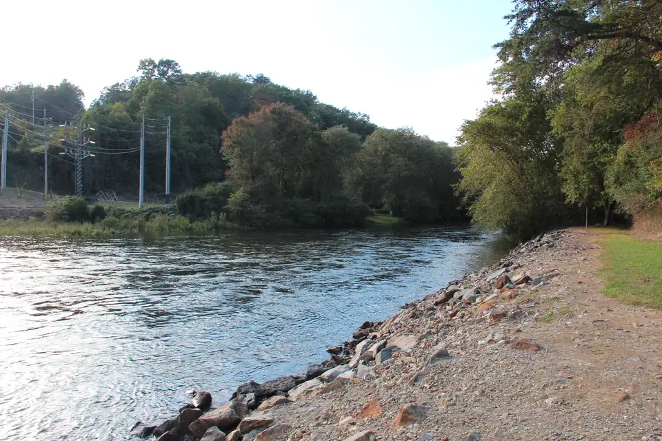 Wide clear river curving past a rocky gravel bank, wooded hills with first fall color, and blue power-line towers on the far bank